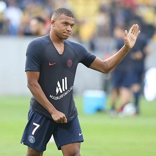 A young Kylian Mbappé in a PSG training kit waving to fans