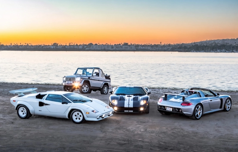 Doug DeMuro's verified garage lineup: white Lamborghini Countach, blue Ford GT, silver Porsche Carrera GT, and Mercedes G500 Cabriolet at sunset
