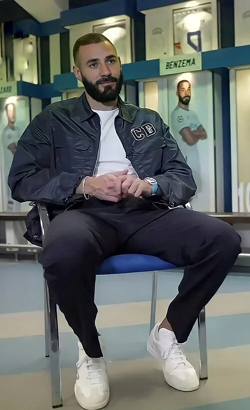 Karim Benzema sitting in the Real Madrid dressing room wearing his CB-branded jacket