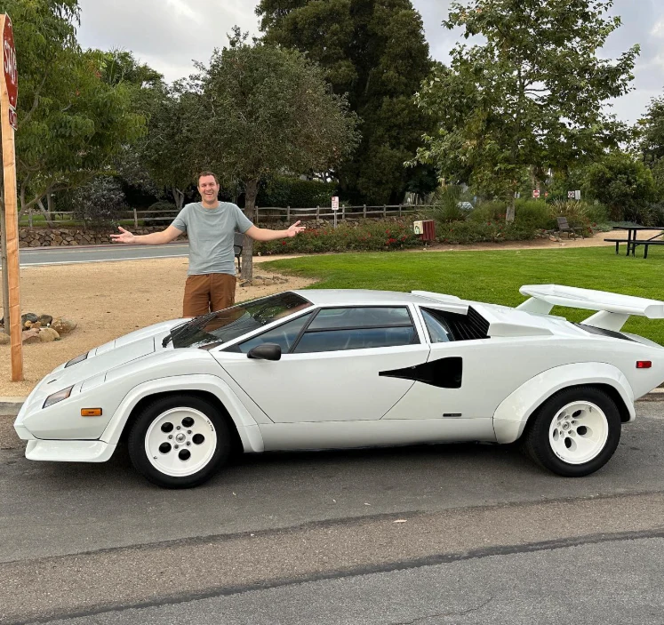 Doug DeMuro posing with a white Lamborghini Countach during a car review, from his official Instagram