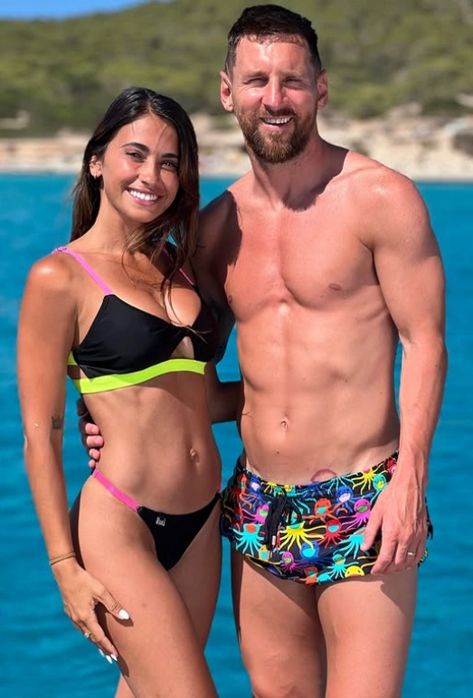 Lionel Messi and Antonela Roccuzzo smiling together in swimwear during a beach vacation.