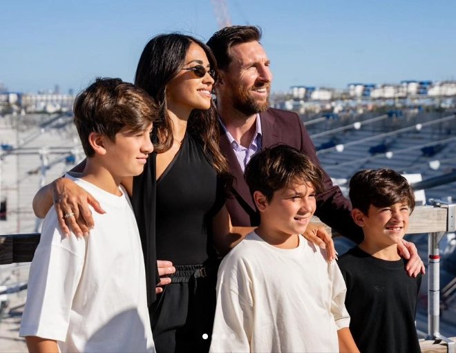 Antonela Roccuzzo and Lionel Messi with their three sons at an outdoor stadium event.