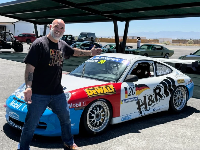 Matt Farah standing next to a Porsche 911 race car at a track event